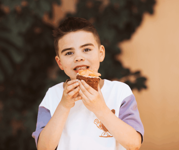 Child enjoying a slice of homemade carrot cake topped with orange icing made from fresh So Sweet carrots.