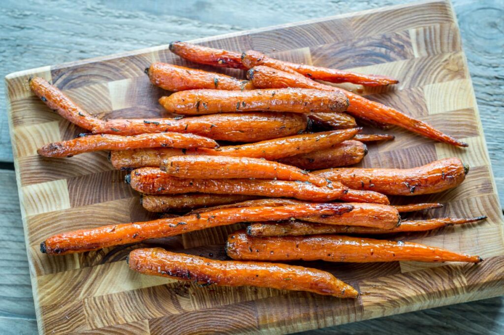 Maple glazed bunch carrots on wooden board with syrup in glass jar