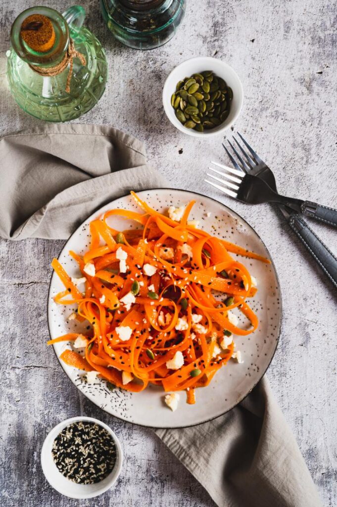 Top view of carrot ribbon salad on a ceramic plate with pumpkin seeds and black and white sesame seeds.
