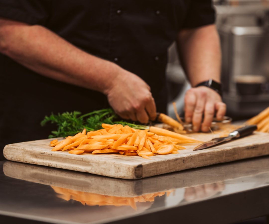 Chef preparing freshly cut carrots in a commercial kitchen, demonstrating food service collaboration with So Sweet produce