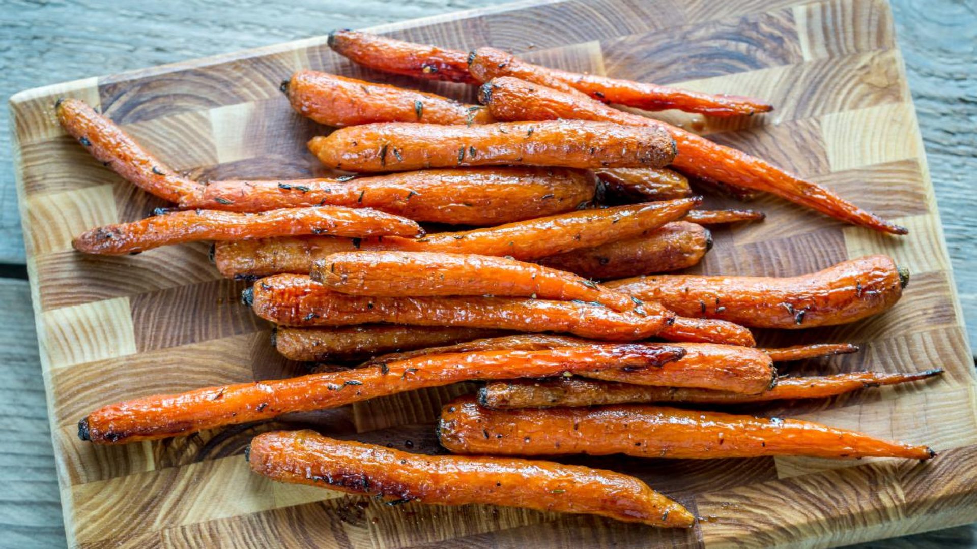 Maple glazed bunch carrots on wooden board with syrup in glass jar
